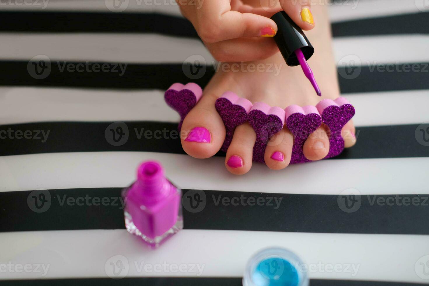 The child paints his toenails with bright purple varnish. Little girl does a pedicure. Beauty salon game. Children's entertainment. photo