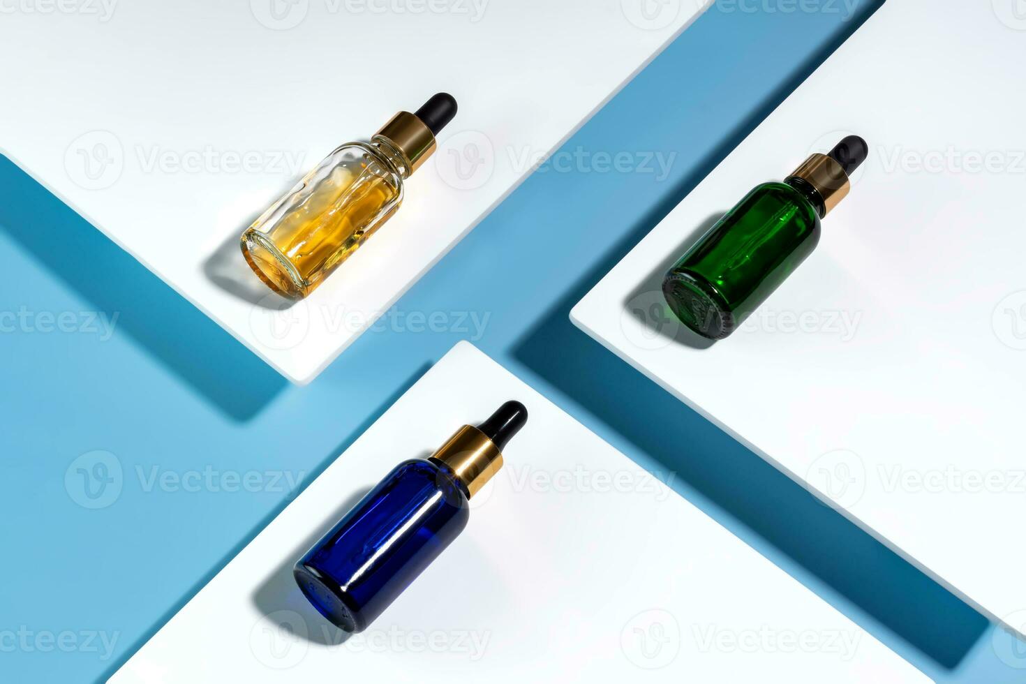 Face serum dropp bottles on white podiums on blue background. Home routine skin care cosmetic set. Unbranded bottles for your design. photo
