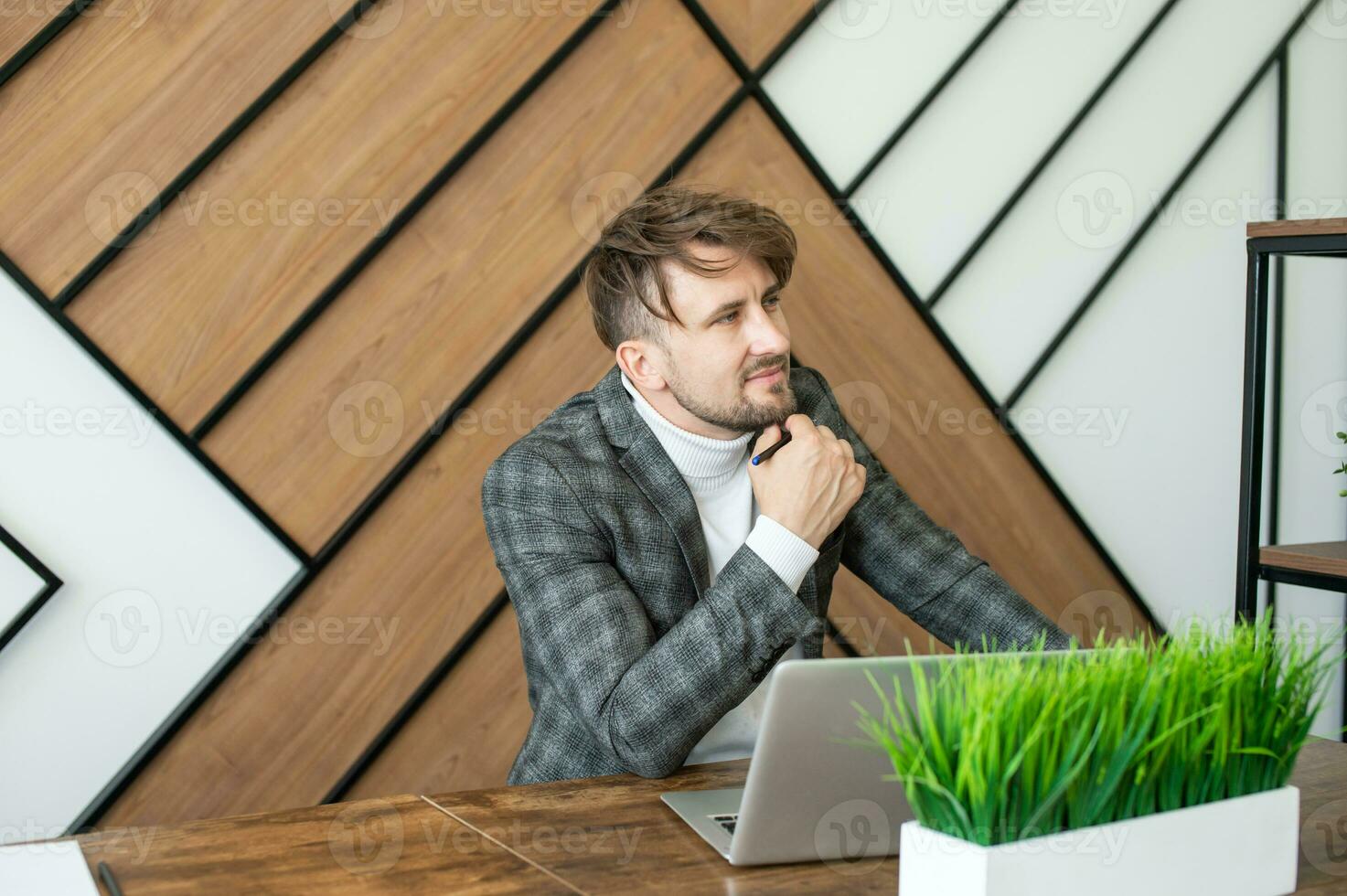 A cheerful man in a jacket sits at his desk in the office and emotionally discusses issues with a colleague photo