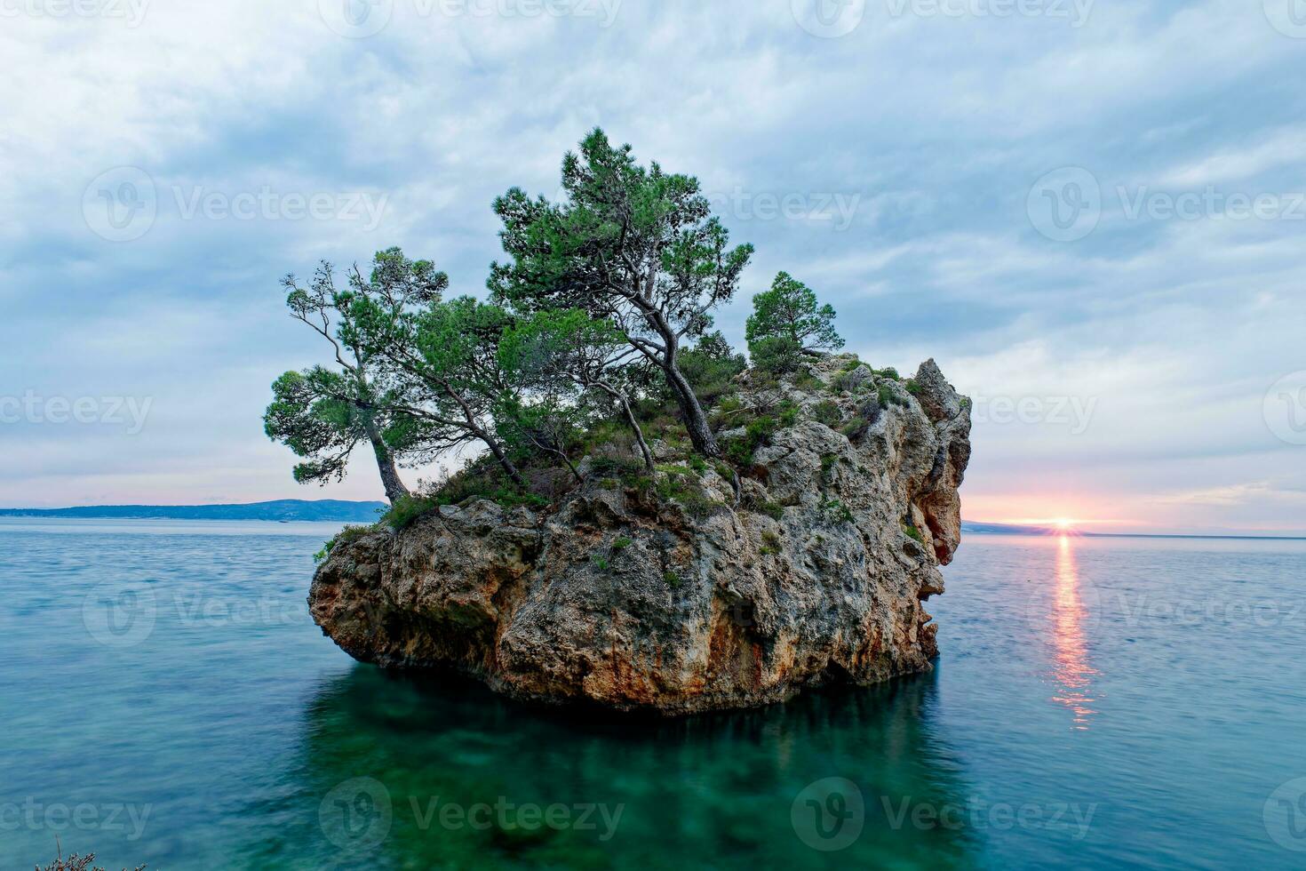The symbol of Brela, The Brela Stone during sunset. This rock in the sea, overgrown with pines, shows the strength and power of survival and growth from the stone itself. Natural beauty. photo
