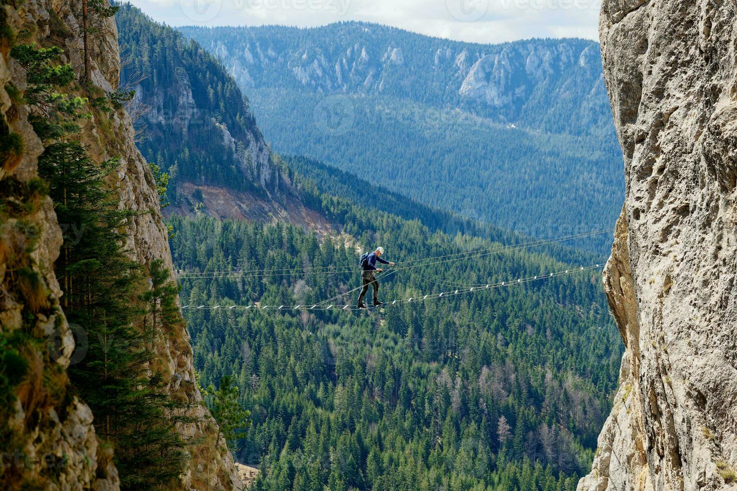 A person passing a via ferrata bridge route between two cliffs. Sports life in the mountains. Active life. Climber using proper equipment for security. Via Ferrata Sokolov put Romanija in BiH. photo