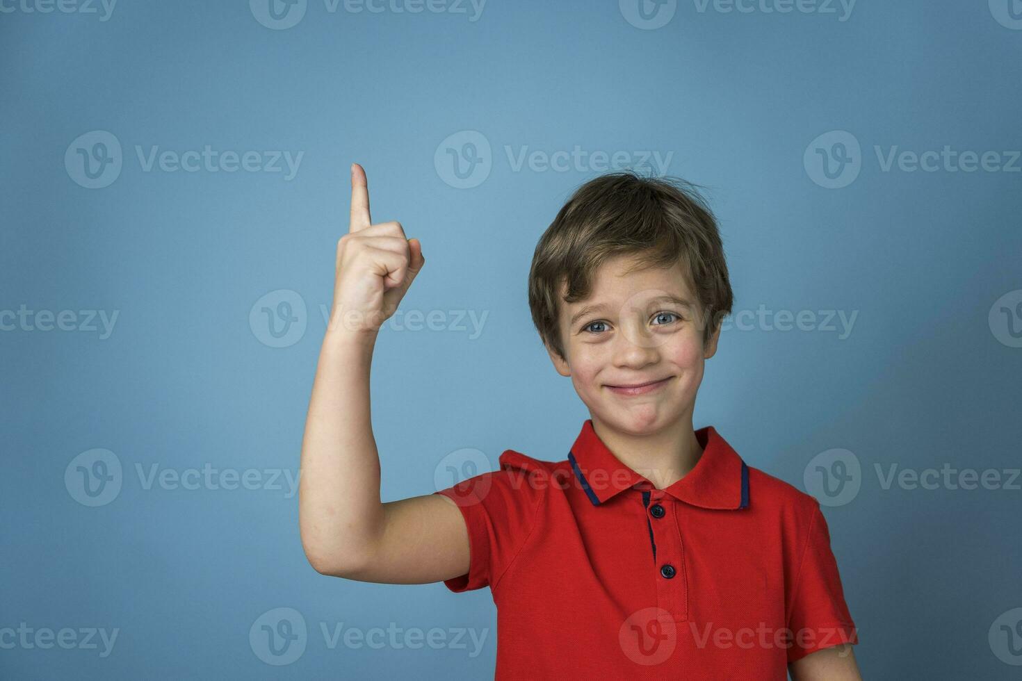 A cute Caucasian boy of 5 years old in a red T-shirt affirmatively and cheerfully points his finger up photo