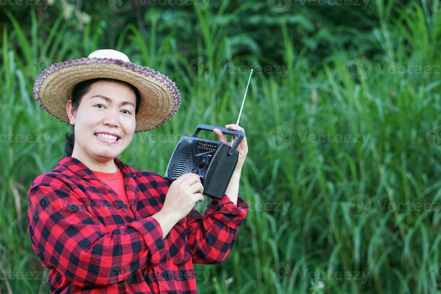 Asian woman farmer, holds AM, FM transistor radio receiver on shoulder. Concept  Happy working along with music, news, information ,advertisement from radio. Country lifestyle. Analog technology. photo