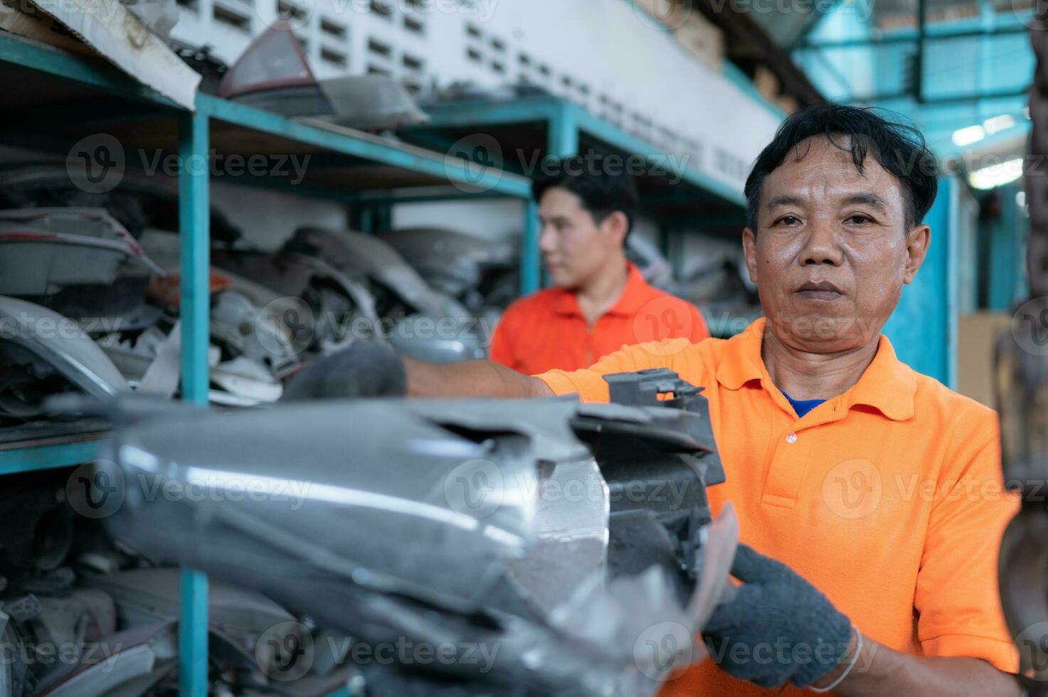 Two mechanics are selecting automobile parts, car headlights, from a spare parts warehouse in order to replace a collision's damaged headlights photo
