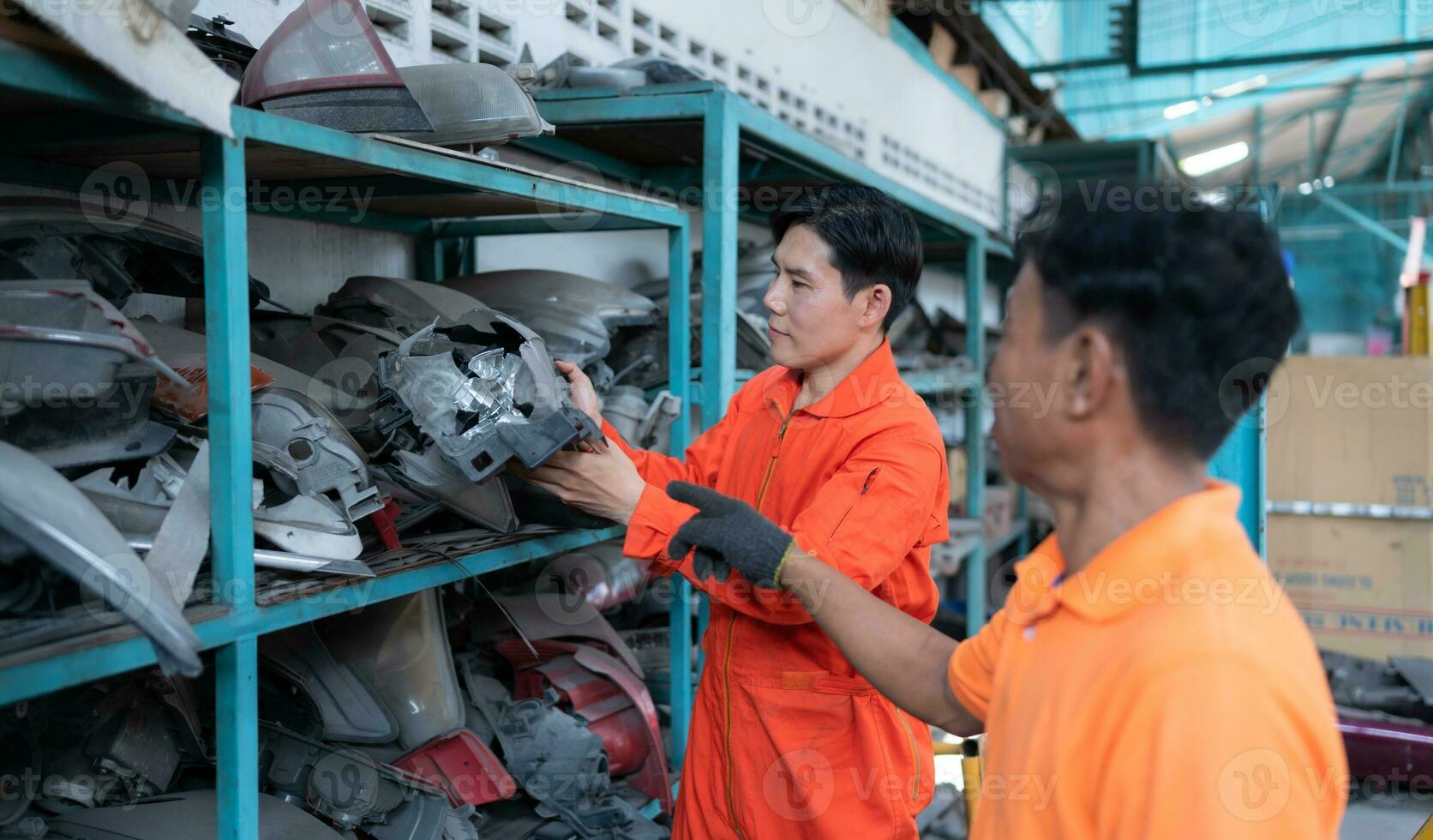 Two mechanics are selecting automobile parts, car headlights, from a spare parts warehouse in order to replace a collision's damaged headlights photo