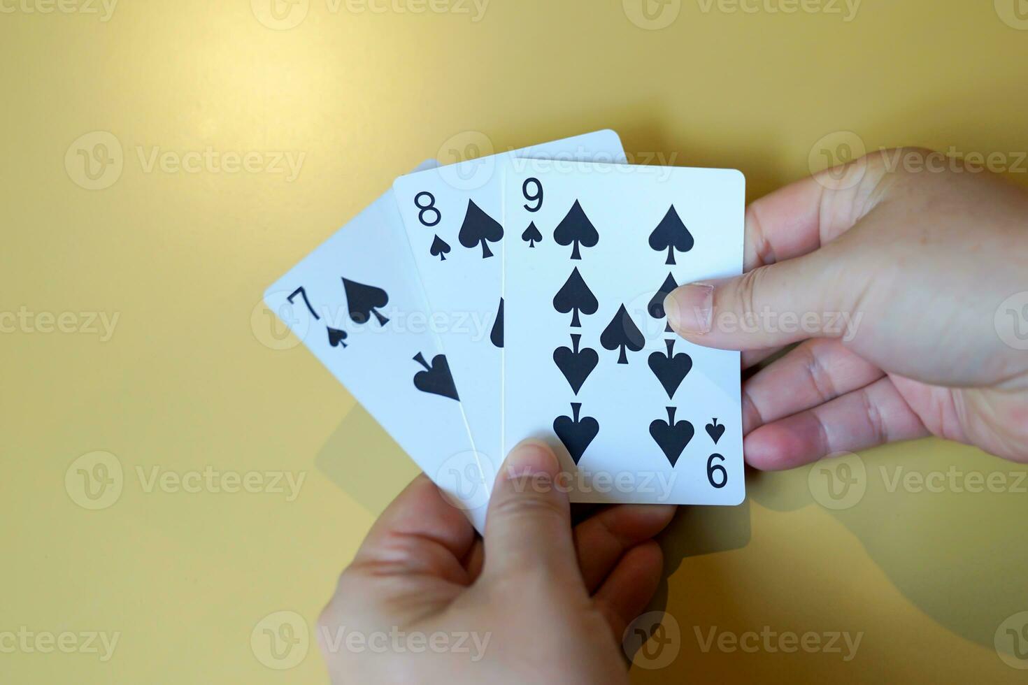 close up of cards in hand There are spade cards in a row of 7, 8 and 9 on a yellow background in the concept of leisure activities, gambling,family activities, group games, group activities. photo