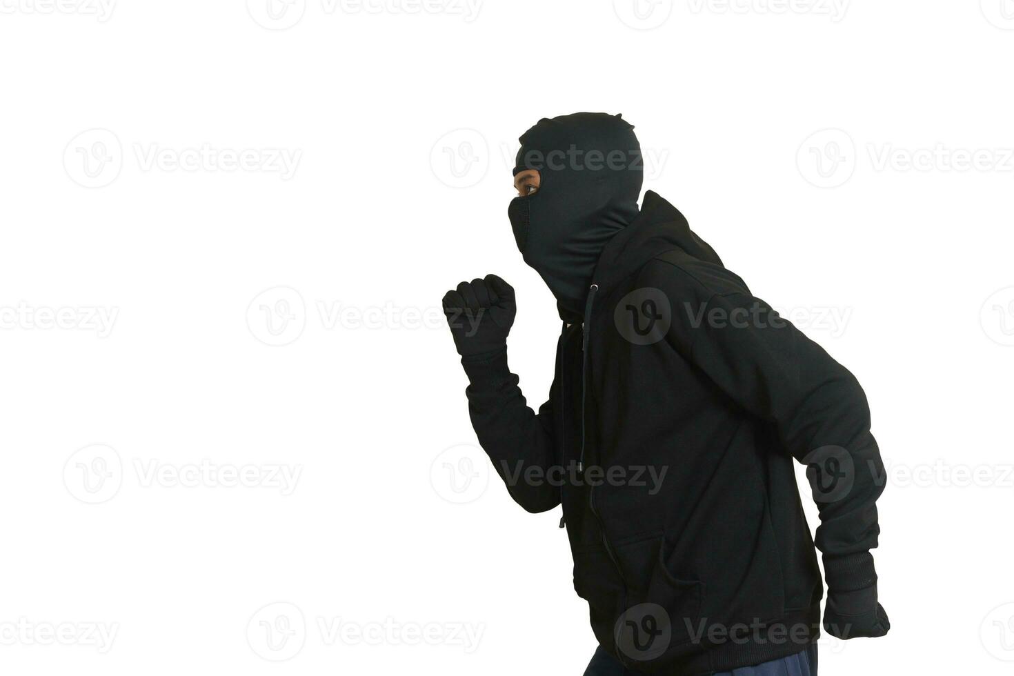 Side view portrait of a masked thief wearing black hoodie sneaking forward and walking slowly. Isolated image on white background photo