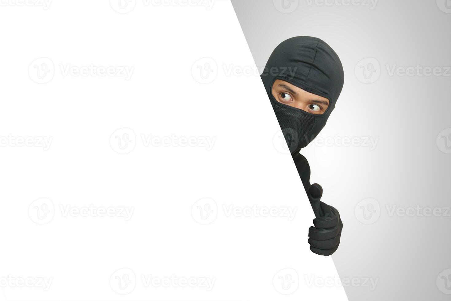 Mysterious thief wearing black hoodie hiding behind wall, sneaking, and looking for stolen goods. Crime concept. Isolated image on gray background photo