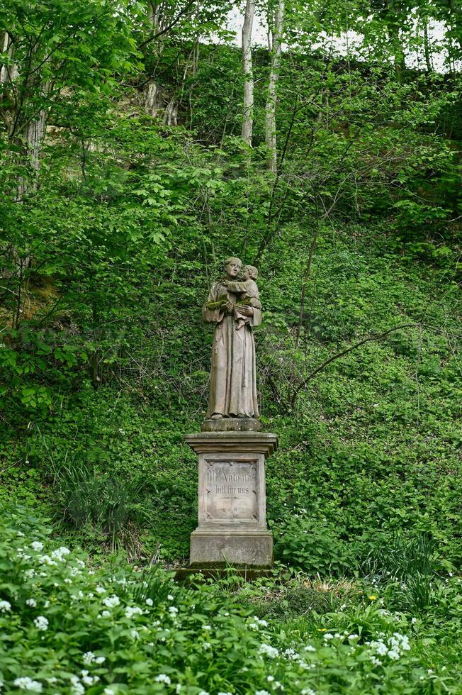 Old stone figure of Saint Antonius deep in the forest on the edge of a Black Forest hiking trail. Germany photo