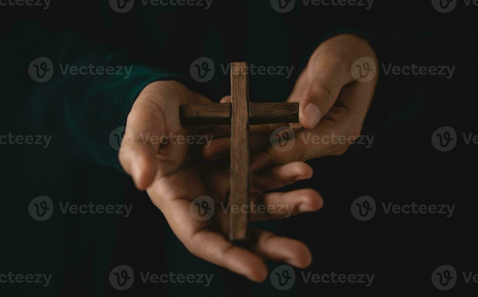Spirituality, Religion and Hope Concept. Person with Wooden Cross on Hands. Symbol of Humility, Supplication, Believe and Faith for Christian People. Dark Tone. Cropped and Selective focus photo