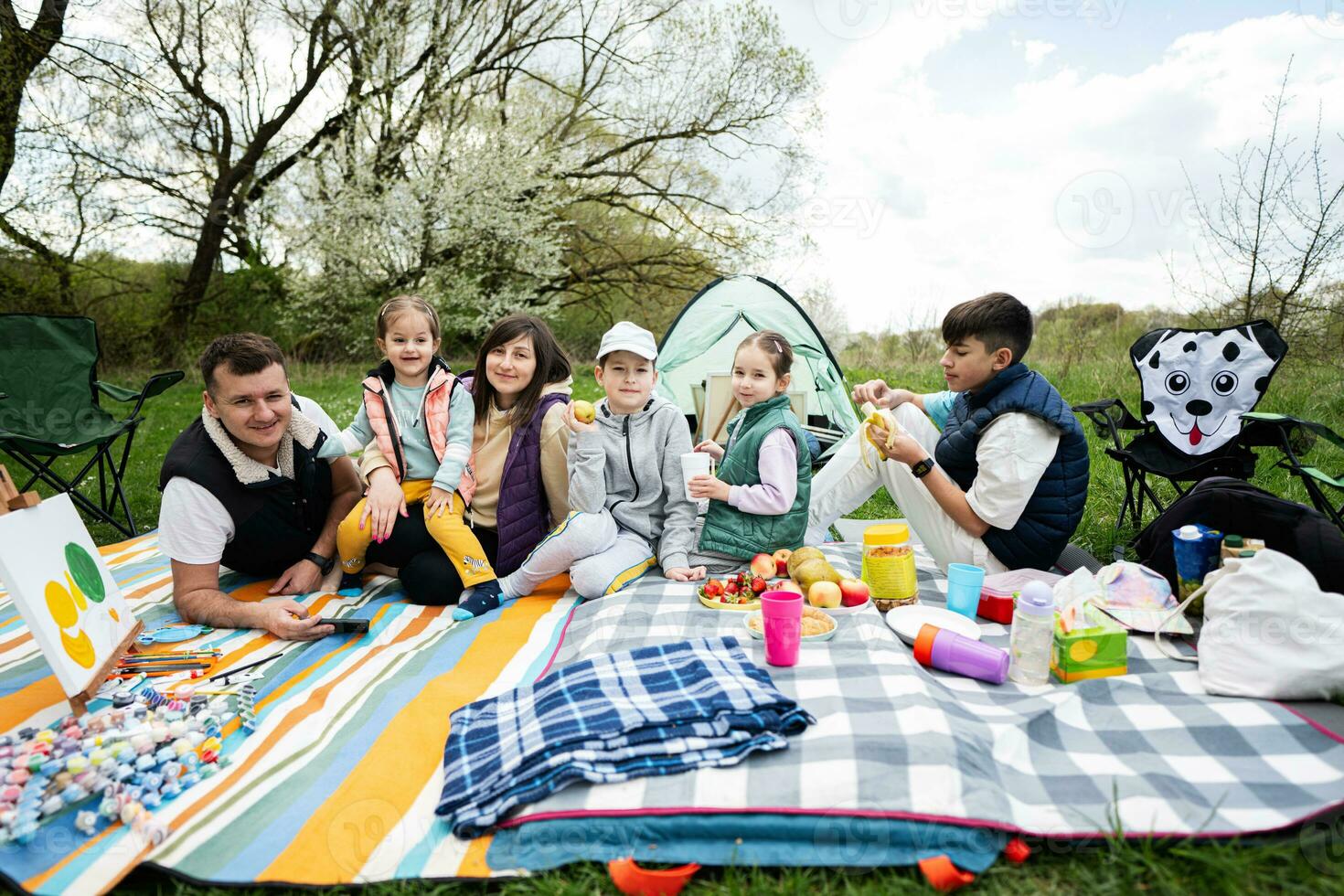 contento joven grande familia con cuatro niños teniendo divertido y disfrutando al aire libre en picnic cobija a jardín primavera parque, relajación. foto