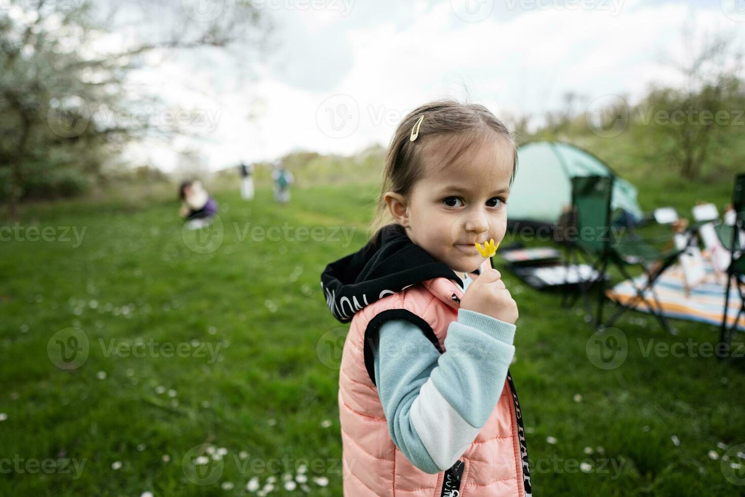 Baby girl sniffs a yellow flower on spring meadow. photo