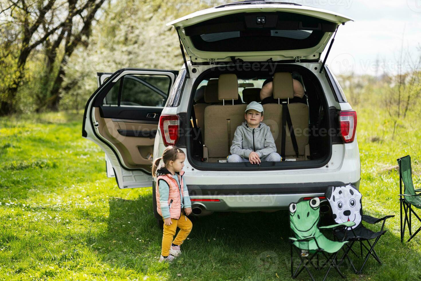 Brother with sister sit on car open trunk at picnic. photo