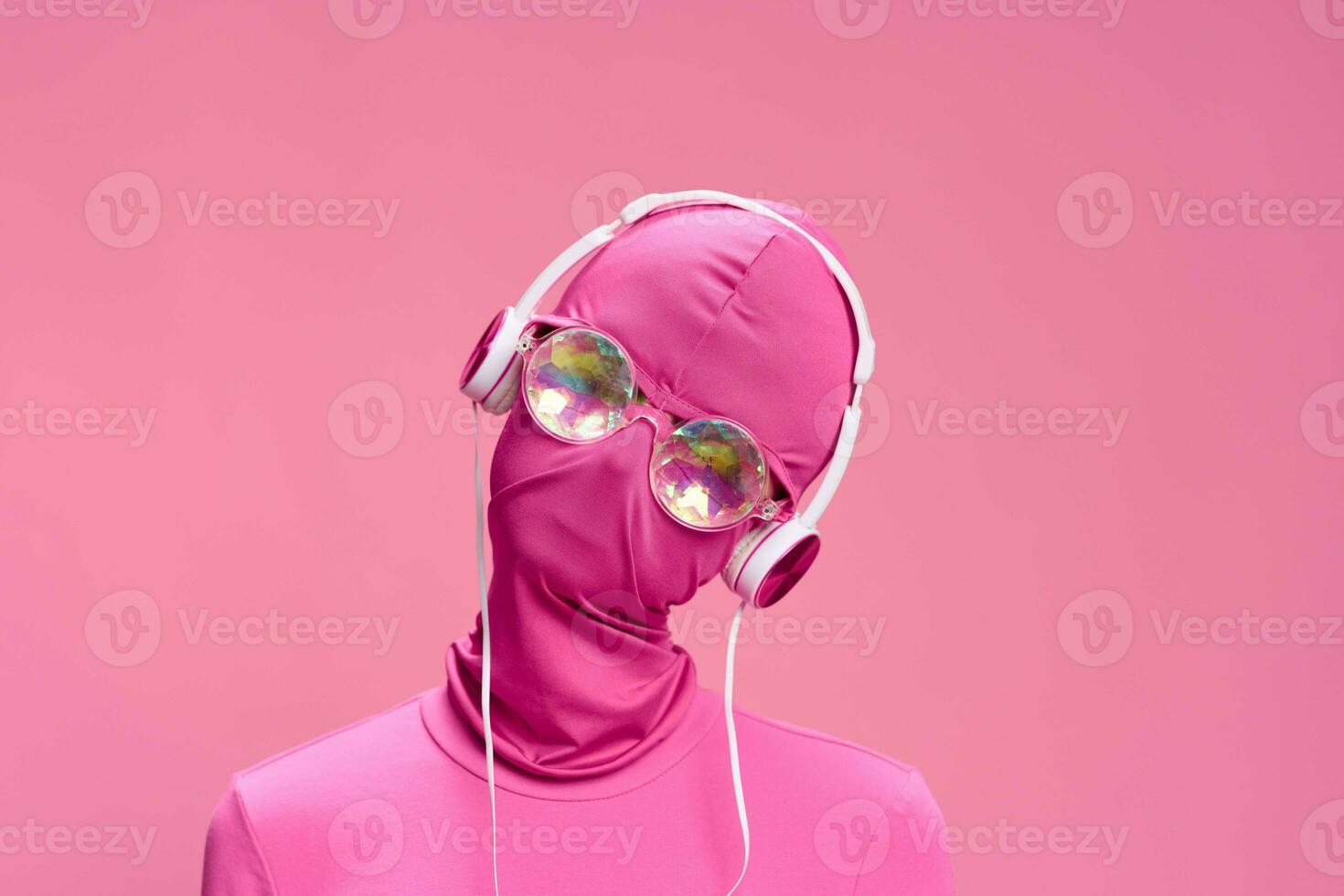 Portrait of a man wearing a pink full-face incognito mask with headphones and shiny round sunglasses on a pink background. Conceptual Art Photography Total Pink photo