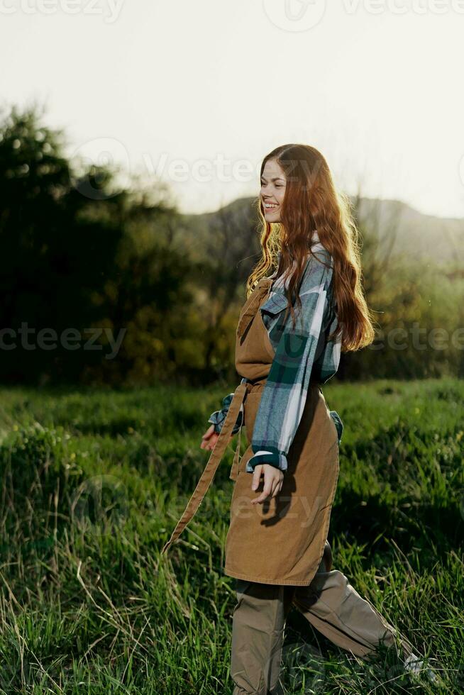 Woman walking on the grass in nature smiling in farm clothes with beautiful hair flying in the wind happy in the rays of summer sunset light photo