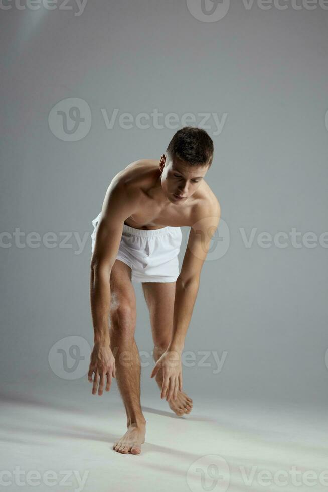 athlete with a pumped-up torso in white shorts on a gray background leaned forward indoors photo