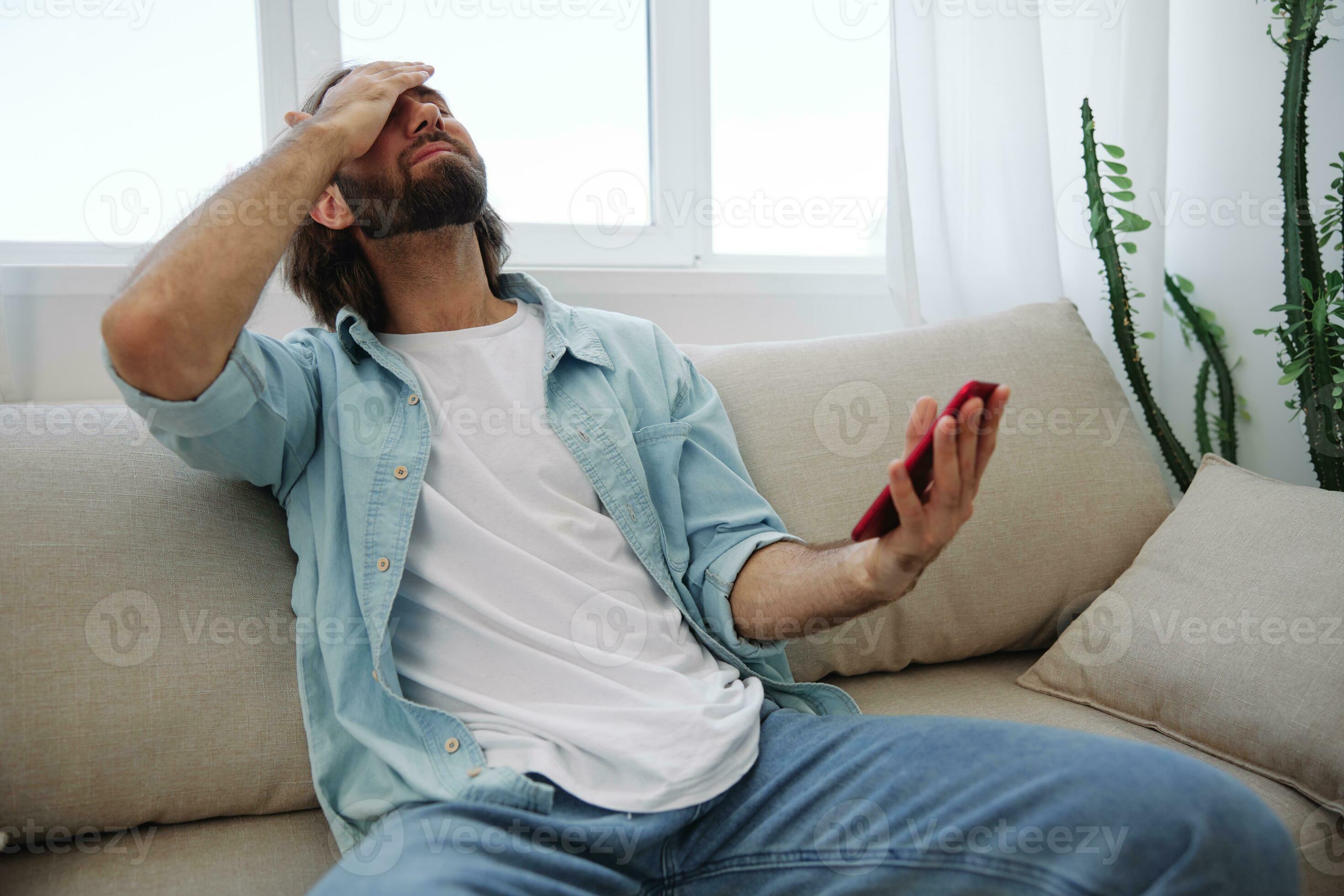A young man looks angrily and sadly at the phone screen at home sitting