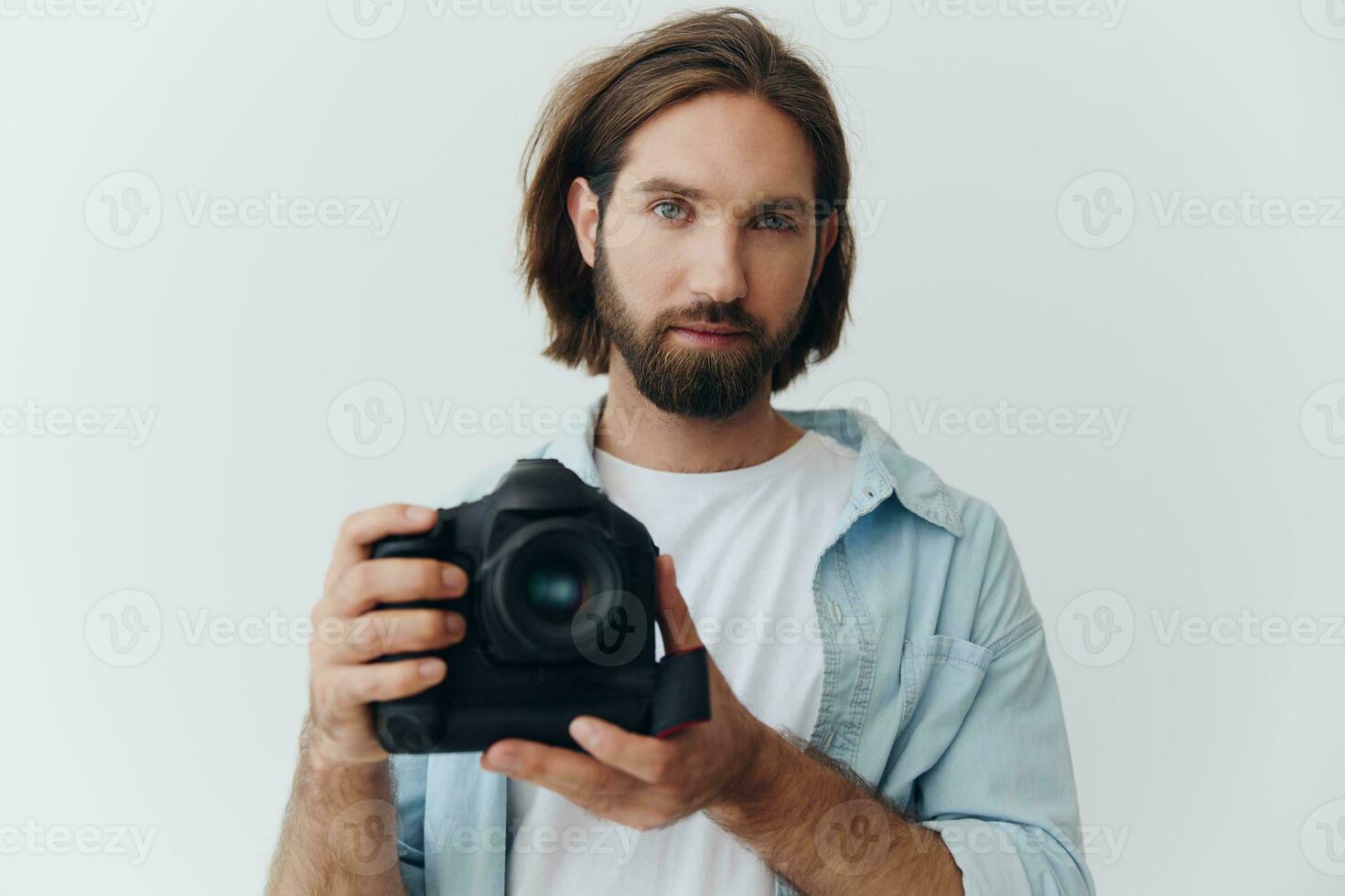 Man hipster photographer in a studio against a white background holding a professional camera and setting it up before shooting. Lifestyle work as a freelance photographer photo