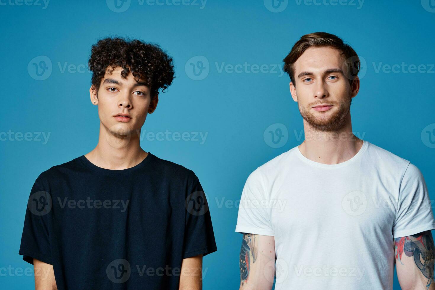 curly guy in a black t-shirt and a man with a tattoo on a blue background friends chatting photo