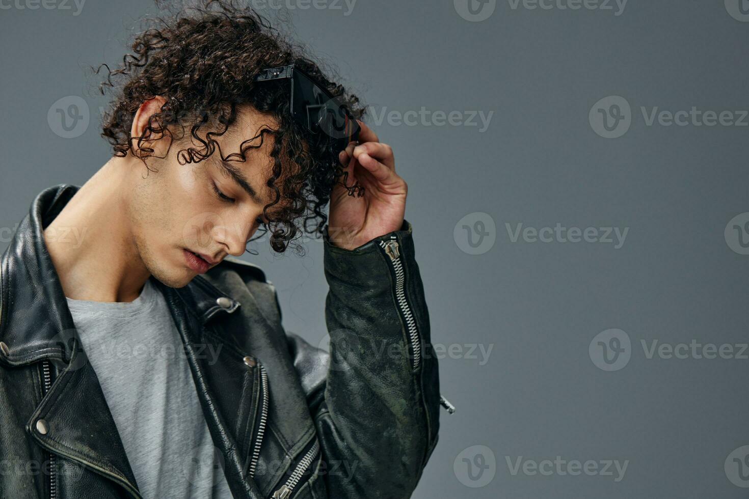 Side of view portrait of stylish tanned curly man leather jacket wear glasses posing isolated on over gray background. Cool fashion offer. Huge Seasonal Sale New Collection concept. Copy space for ad photo