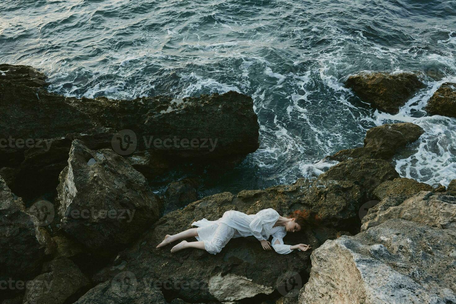 woman in a white dress lying on a stone in a white dress view from above photo