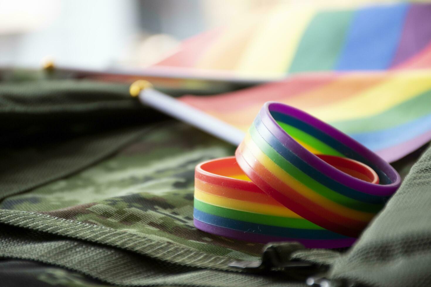 Rainbow flag and rainbow wristbands on camouflage background, concept for celebrations of LGBT people in pride month around the world, soft and selective focus on wristband. photo