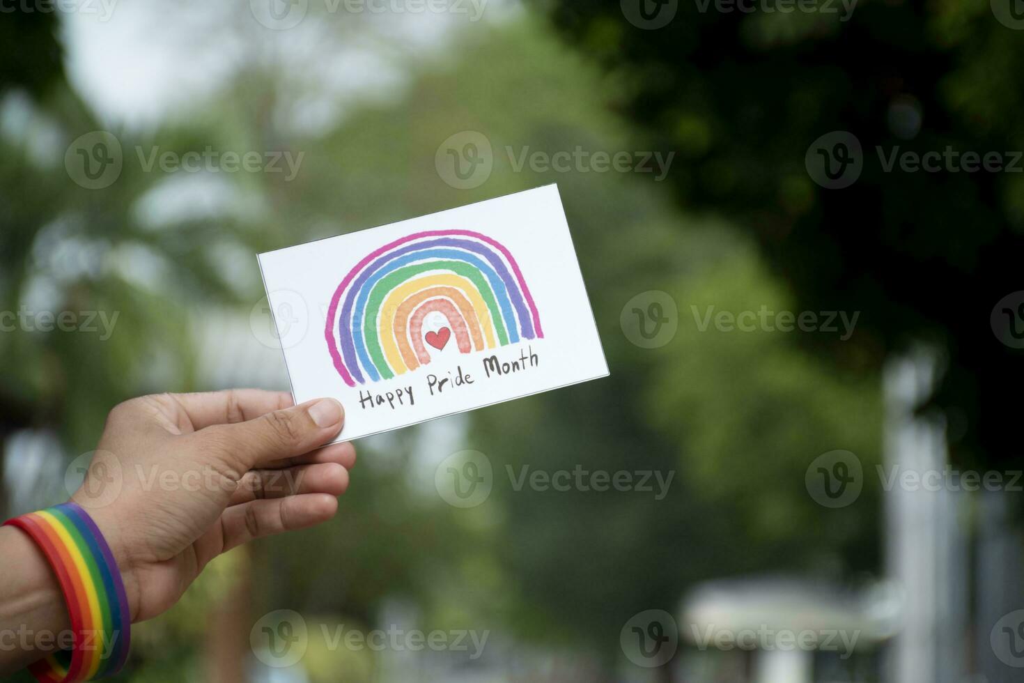 'Happy Pride Month' card holding in hand which has rainbow wristband around it, concept for greeting all people to be happy in the LGBTQ events around the world in pride month. photo