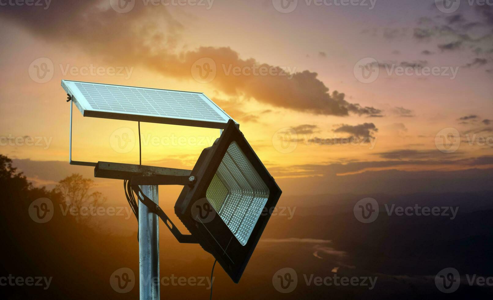 Mini photovoltaic or solar cell panel installed on metal pole with hd floodlight to store and use the power from the sunlight at night around house on the mountain, blurred sunset mountain background. photo