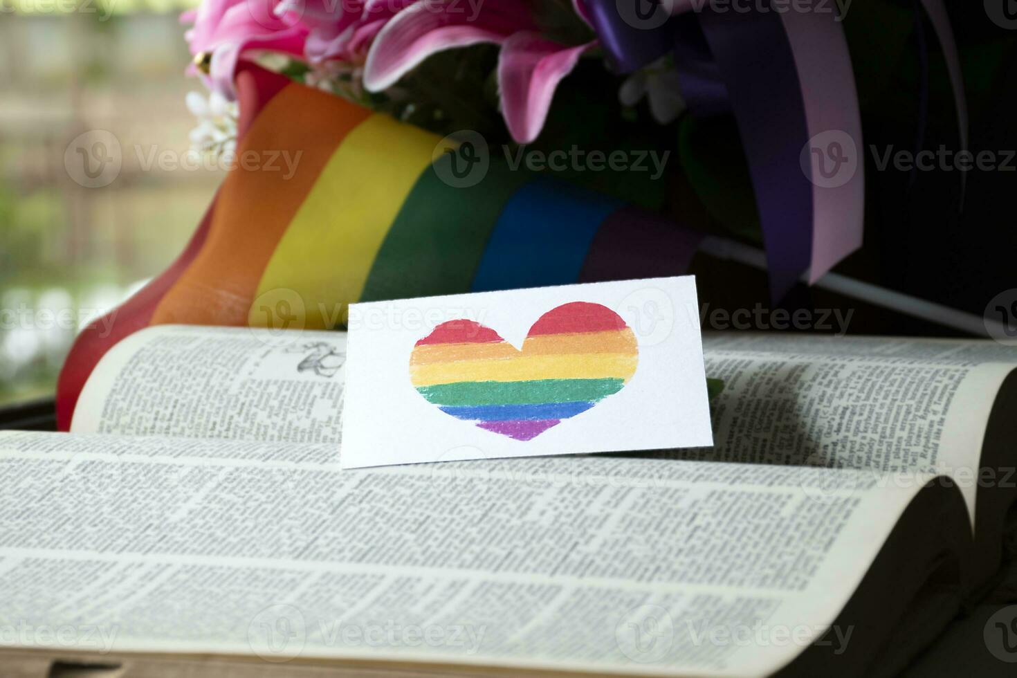 Closeup view of bookmark in heart shape which drew with rainbow colours, blurred opened old book background, concept for calling out all people to respect gender diversity of humans in pride month. photo