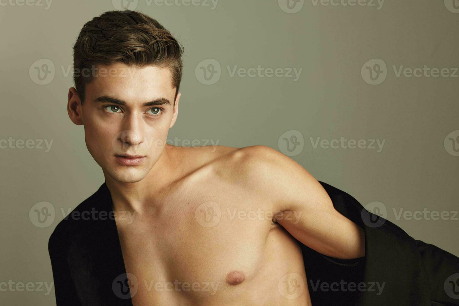 Attractive gentleman with naked shoulders on a beige background with an unbuttoned jacket photo