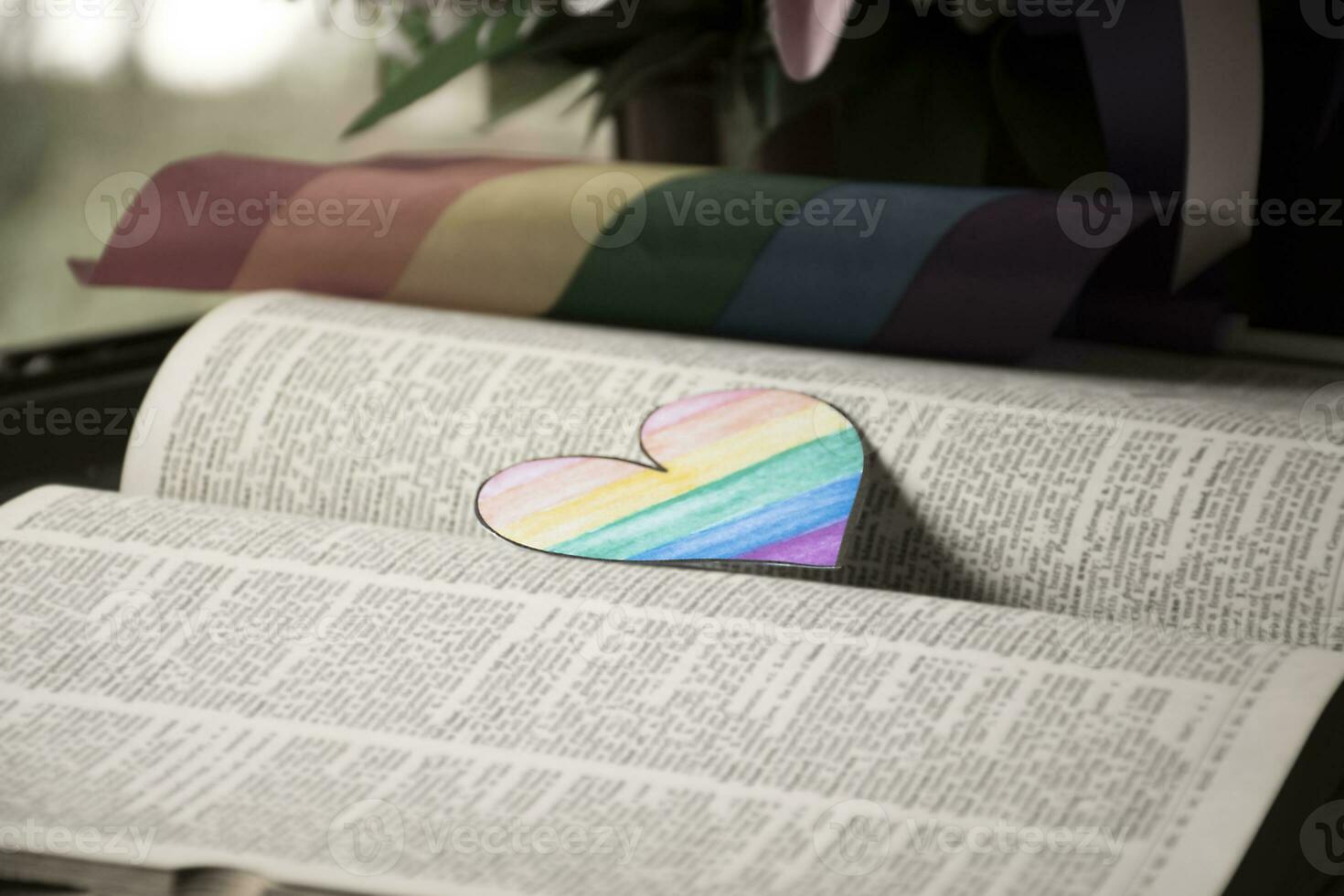 Closeup view of bookmark in heart shape which drew with rainbow colours, blurred opened old book background, concept for calling out all people to respect gender diversity of humans in pride month. photo