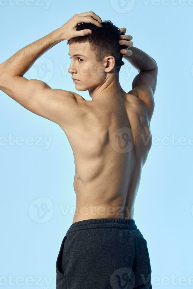a guy with an athletic figure holds his hands behind his head on a blue background bodybuilder sport photo