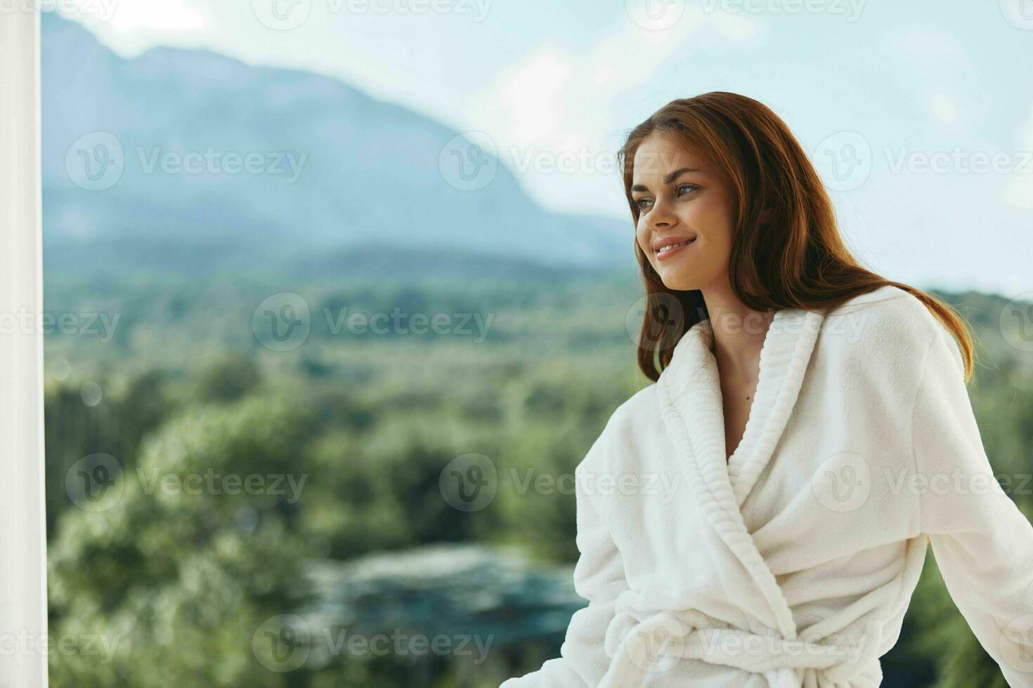 Attractive young woman white robe admire the view from the window Mountain View photo