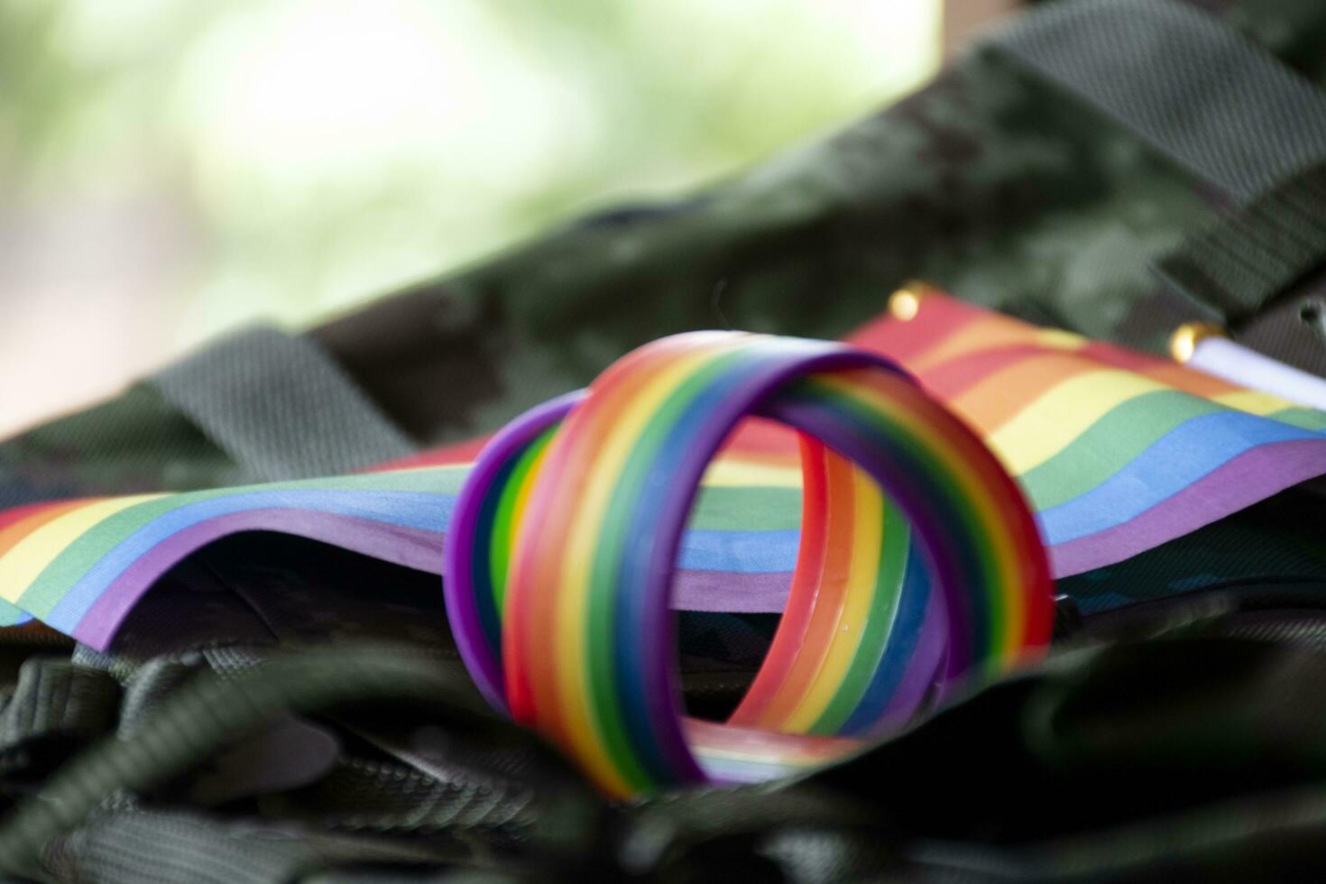 Rainbow flag and rainbow wristbands on camouflage background, concept for celebrations of LGBT people in pride month around the world, soft and selective focus on wristband. photo