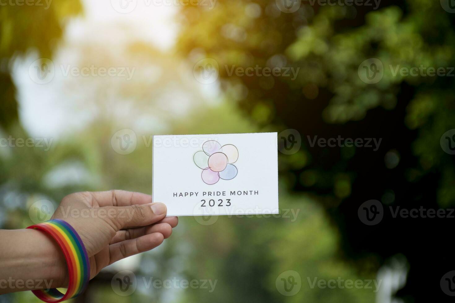 'Happy Pride Month 2023' card holding in hand which has rainbow wristband around it, concept for inviting all people to join the LGBTQ events around the world in pride month. photo