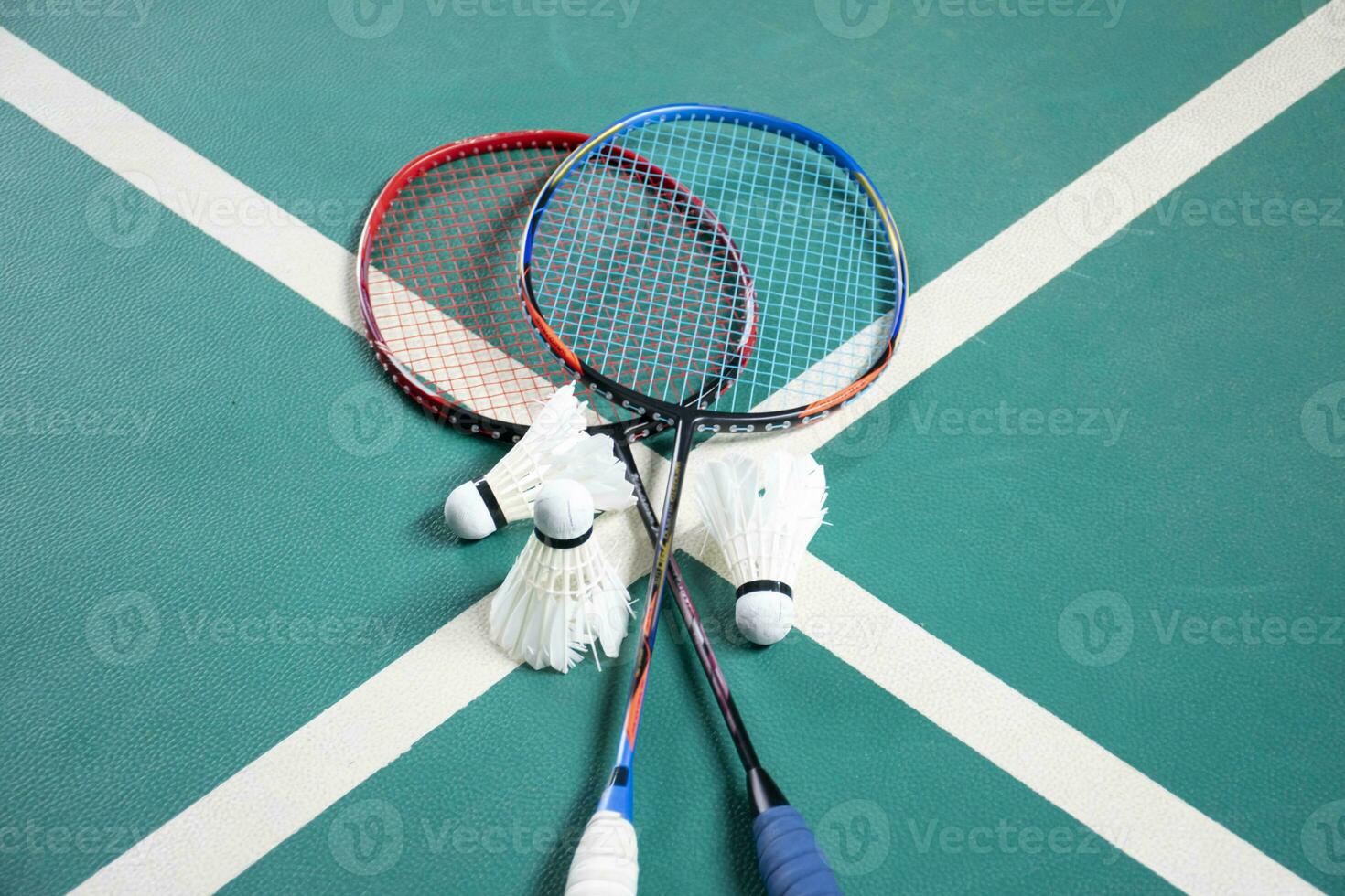 Badminton rackets and white cream badminton shuttlecocks after playing or after games on green floor in indoor badminton court, soft focus, concept for badminton lovers around the world. photo