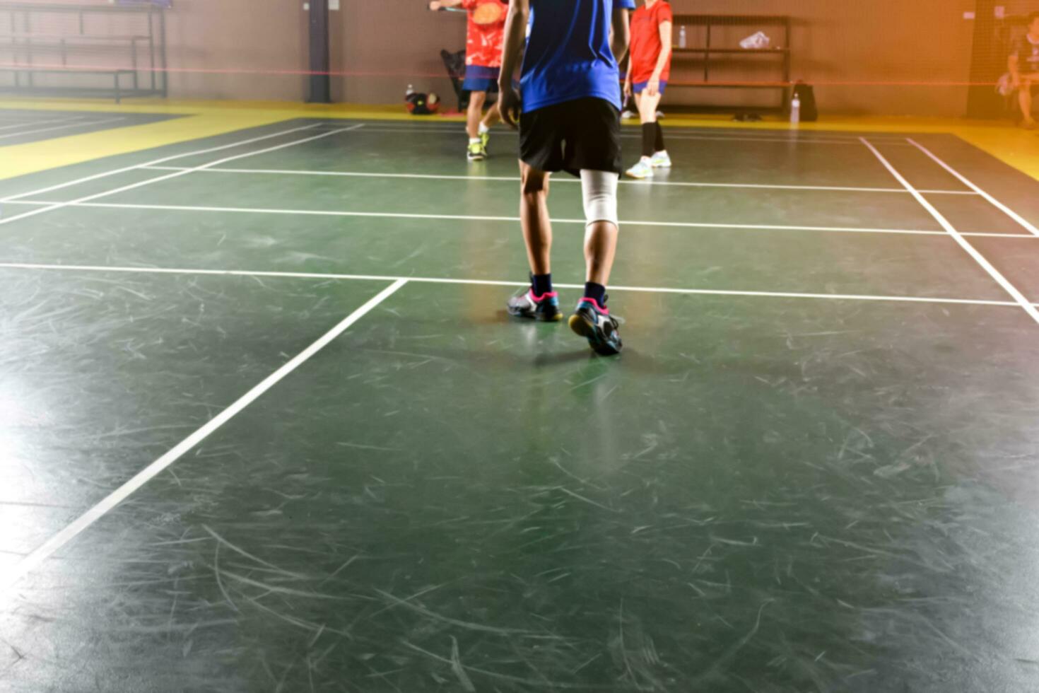 A badminton athlete wraps his right knee with a white knee bandage to support his knee and heal his injury while playing badminton together with his friends in the badminton court. photo