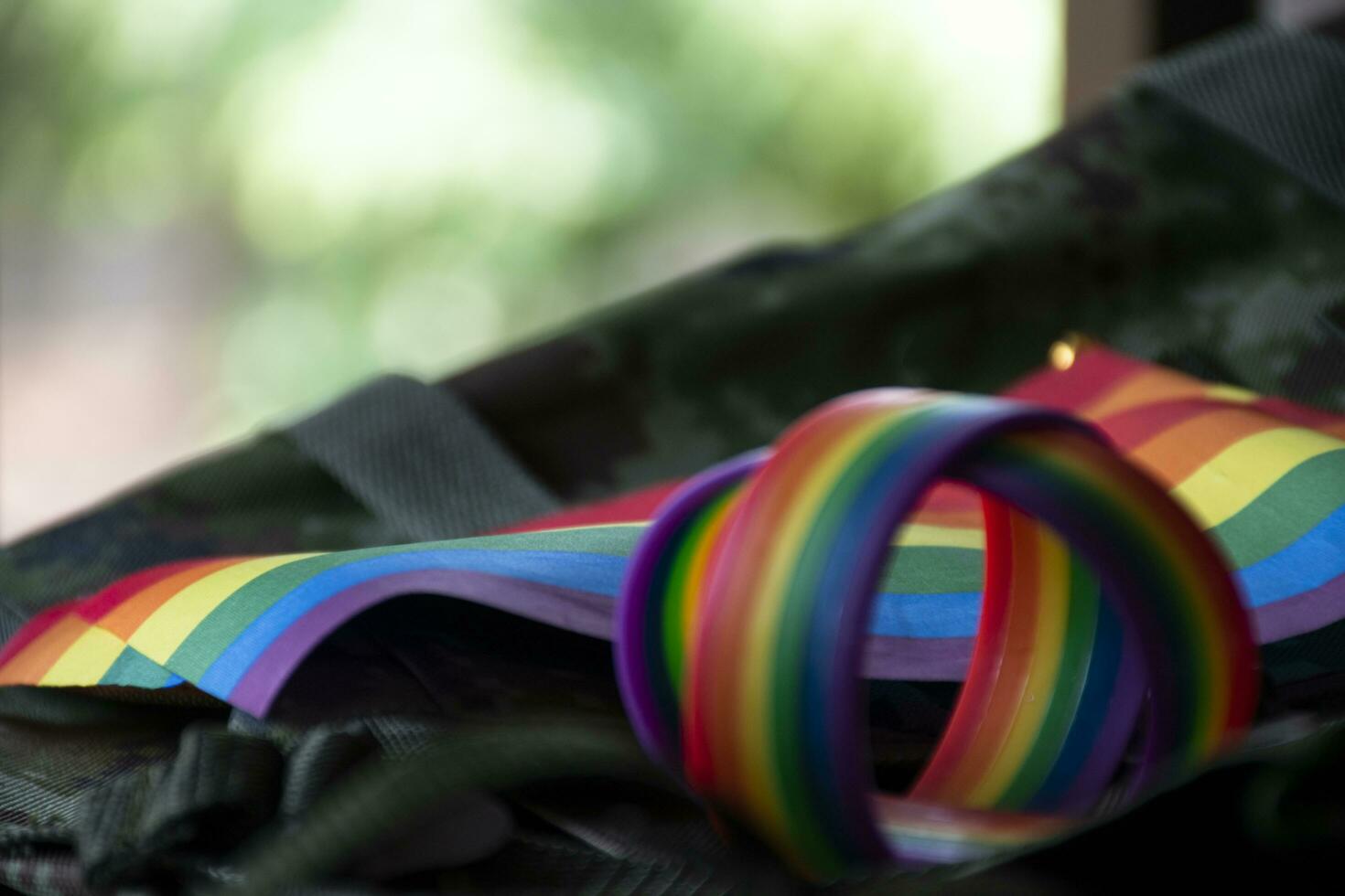 Rainbow flag and rainbow wristbands on camouflage background, concept for celebrations of LGBT people in pride month around the world, soft and selective focus on wristband. photo
