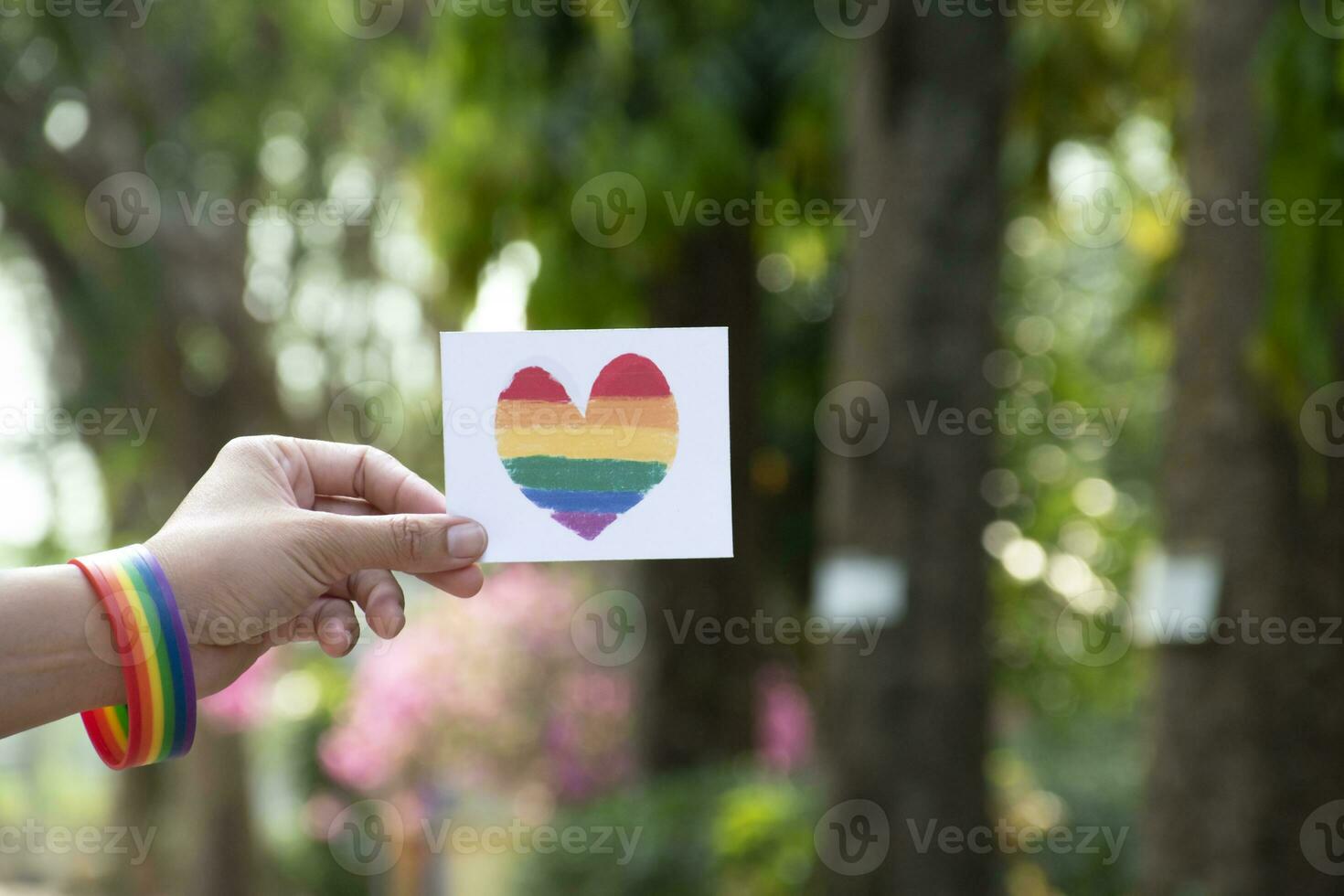 Heart rainbow colours card holding in hand which has rainbow wristband around it, concept for giving love and inviting all people to celebrate LGBT events in pride month. photo
