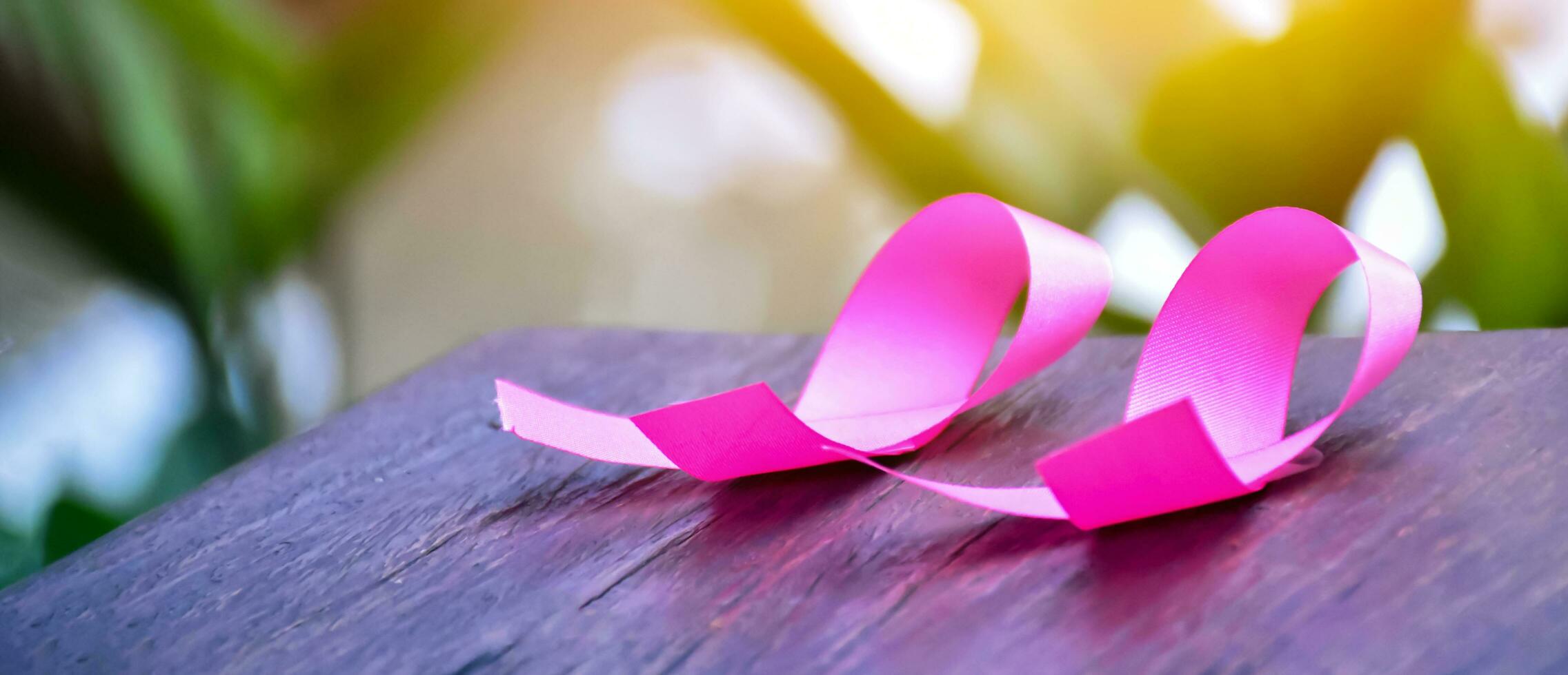 Pink ribbons on wooden table, sunlight and blurred background, concept for breast cancer awareness around the world. Soft and selective focus on pink ribbons. photo