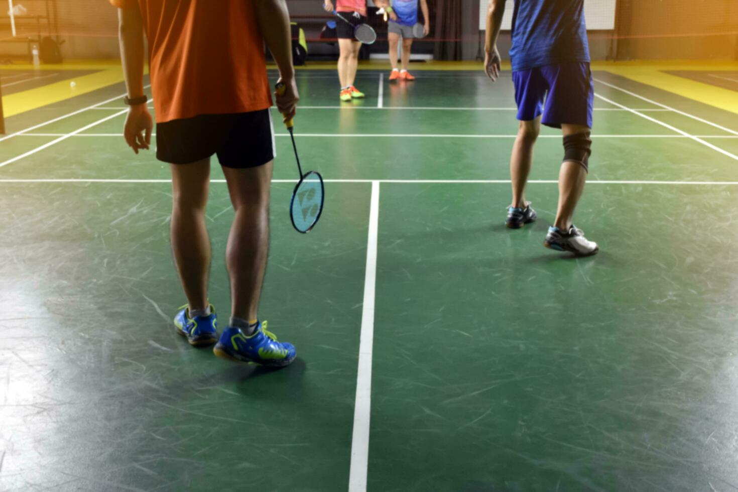 un bádminton atleta envuelve su Derecha rodilla con un blanco rodilla vendaje a apoyo su rodilla y sanar su lesión mientras jugando bádminton juntos con su amigos en el bádminton corte. foto