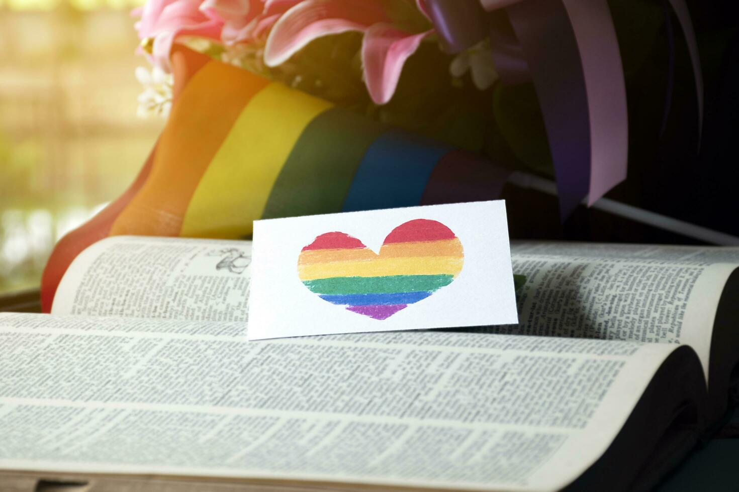 Closeup view of bookmark in heart shape which drew with rainbow colours, blurred opened old book background, concept for calling out all people to respect gender diversity of humans in pride month. photo