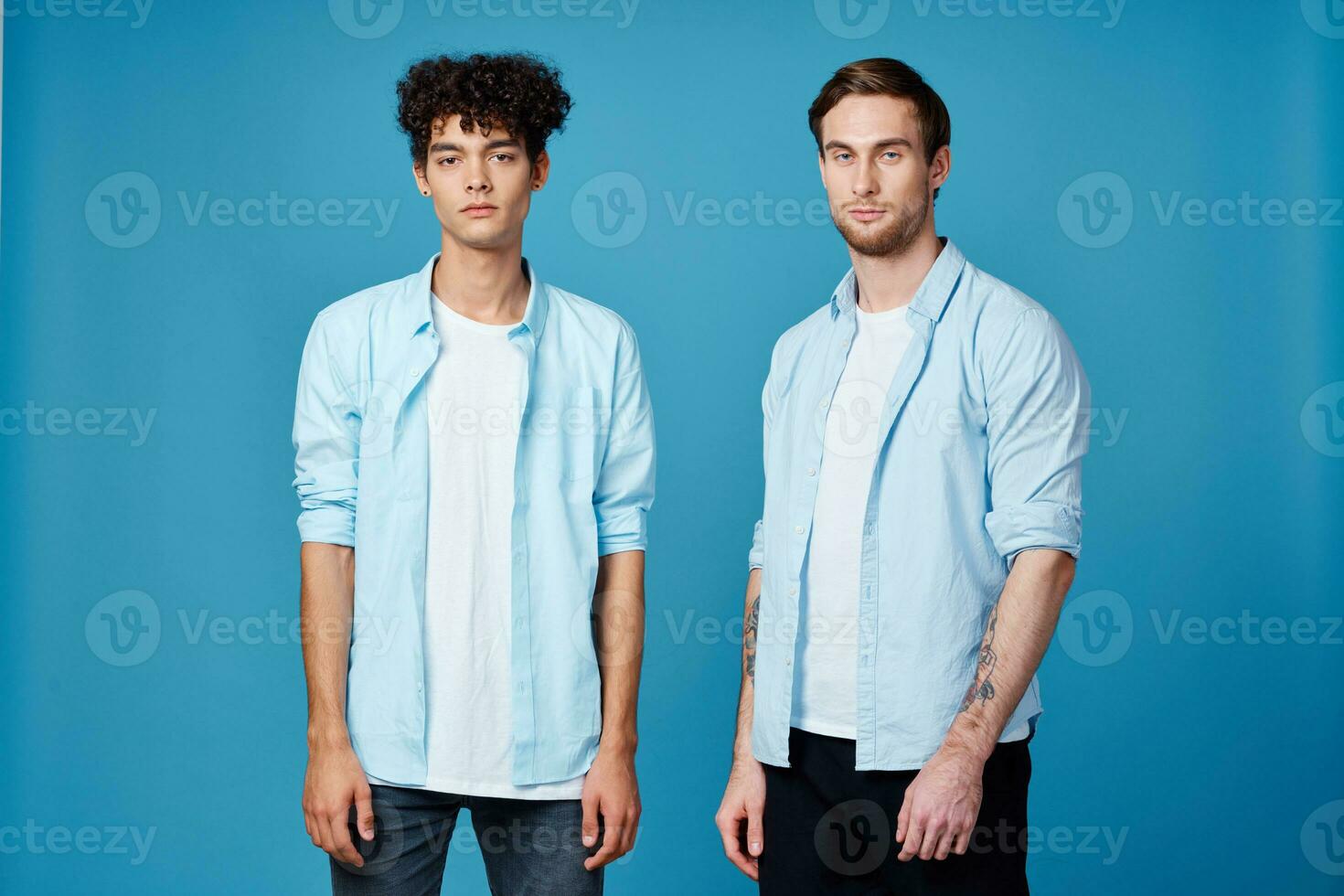 curly guy in a shirt stands next to a young man in a t-shirt on a blue background cropped view photo