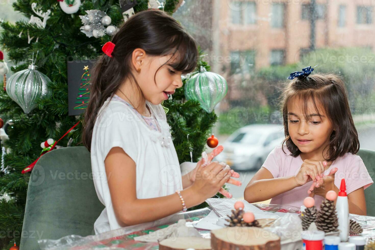 dos pequeño hermanas teniendo divertido mientras haciendo Navidad natividad artesanía con a hogar - real familia foto