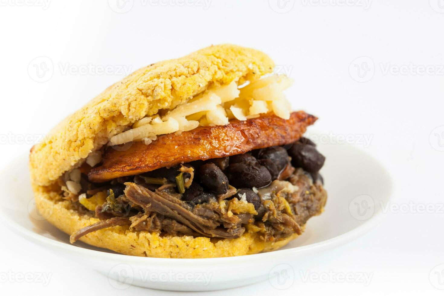 arepas lleno con triturado carne de res, negro frijoles, plátano y queso servido en un blanco plato en blanco antecedentes foto