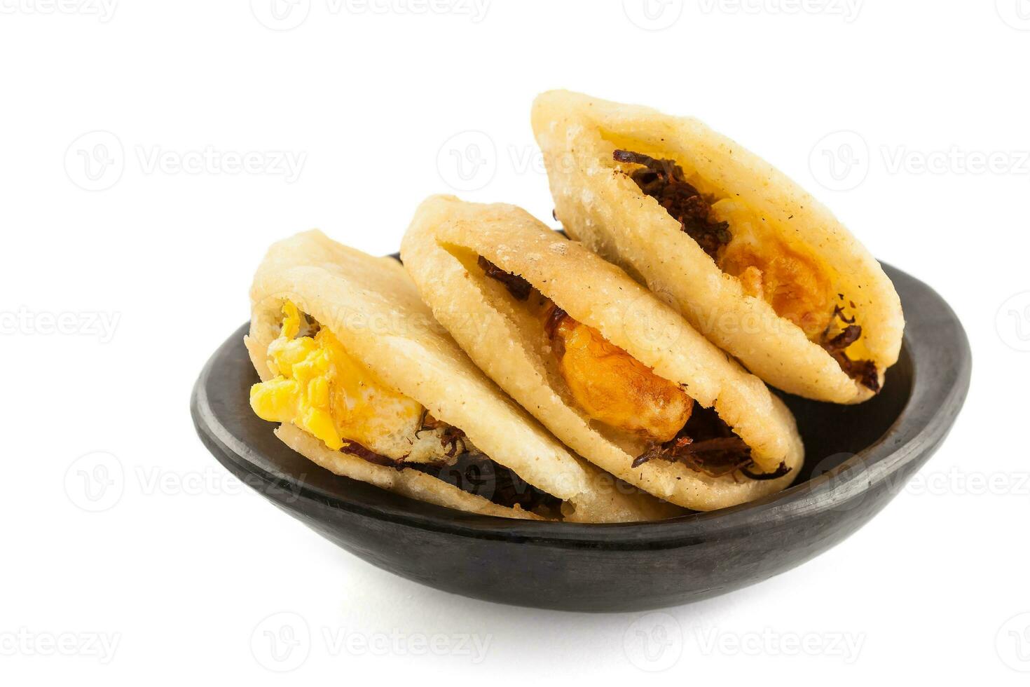 Arepa de huevo. Traditional Colombian fried arepa filled with egg and shredded meat served in a black ceramic dish on white background photo