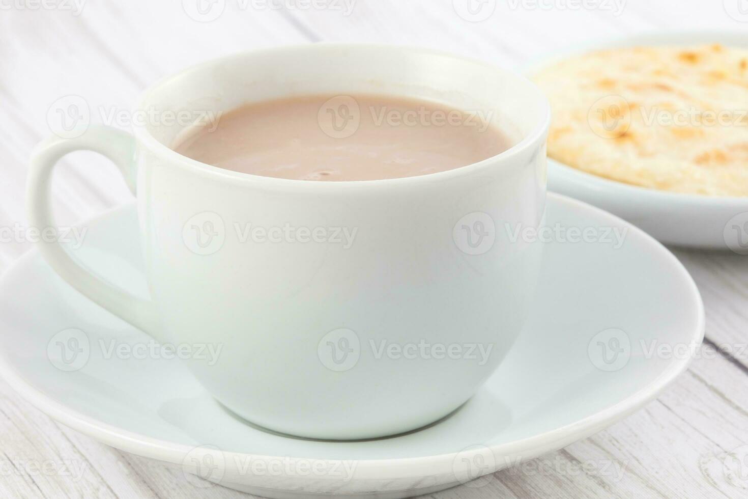 Cup of hot chocolate with cheese and arepa served in white dishware photo