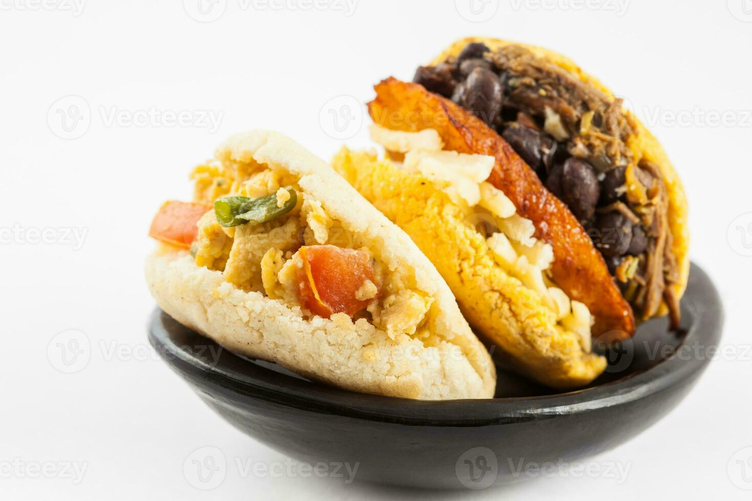 Arepas with two different fillings served in a black ceramic dish on white background photo