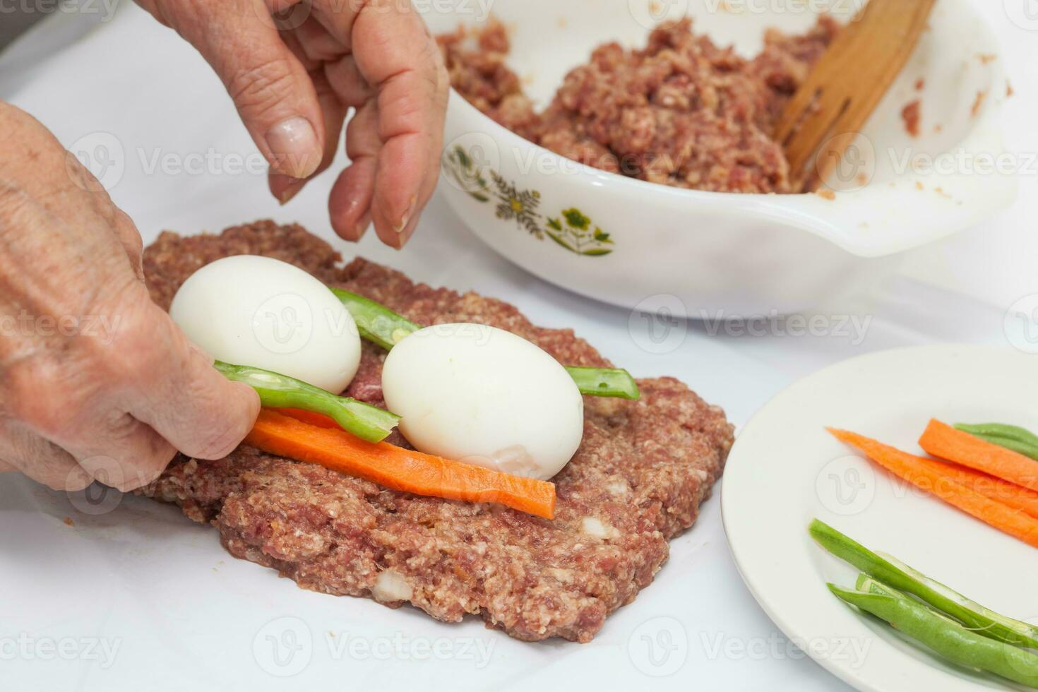 Preparation of a baked egg and vegetables stuffed meatloaf covered with bacon. Meat roll photo