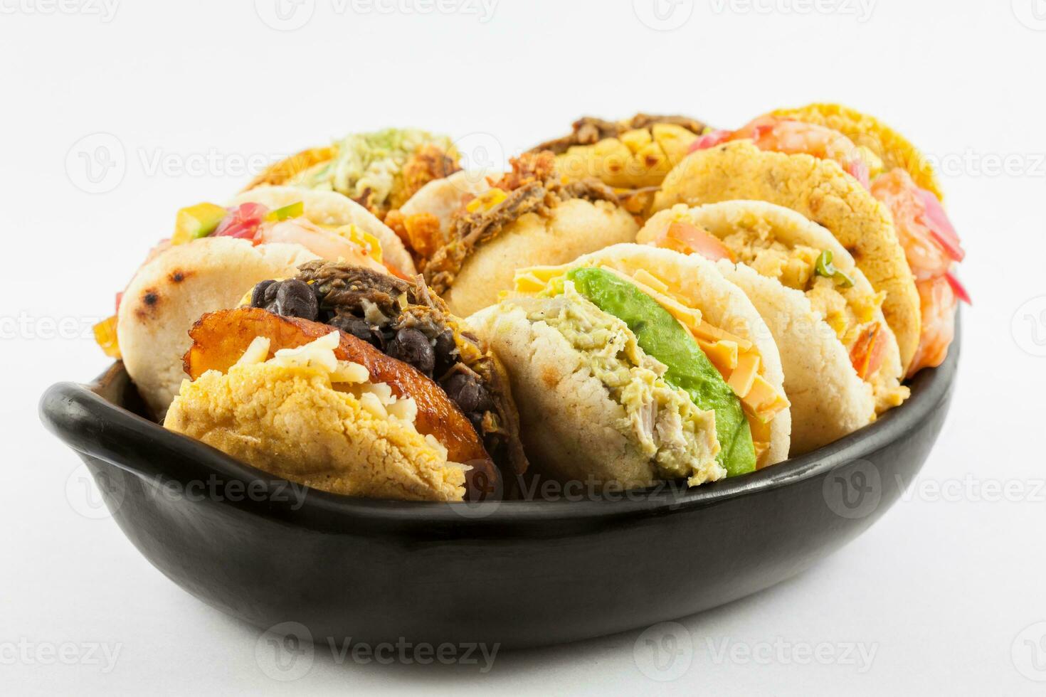 Arepas with assorted fillings served in a black ceramic dish on white background photo